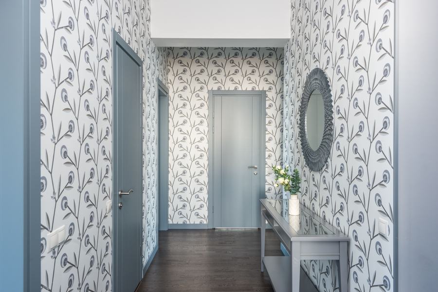 Couloir tapissé de papier peint à motif de feuillage, avec une console et un miroir rond