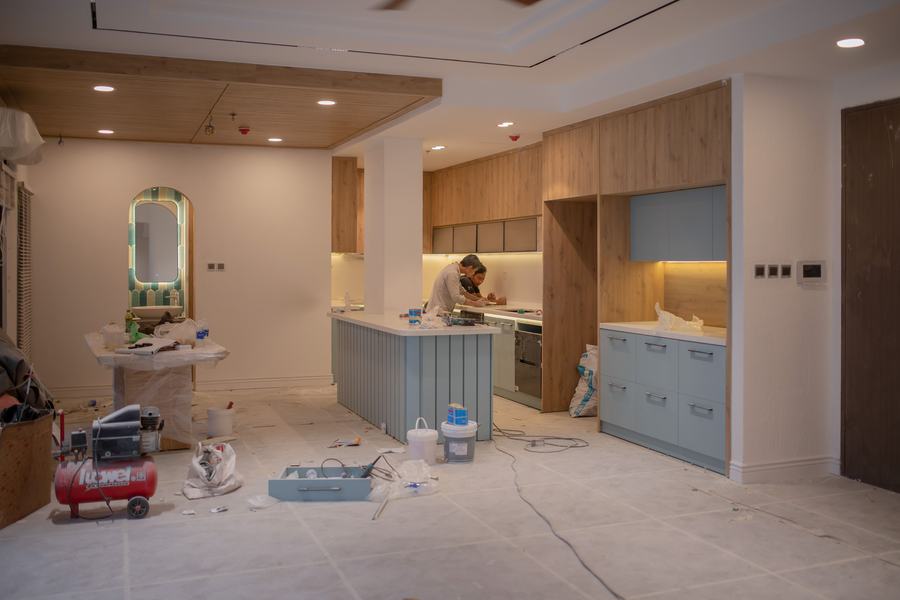 Cuisine en cours de rénovation avec des meubles bleu-gris montés, un îlot et un compresseur au sol