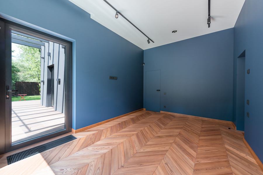 Pièce aux murs bleus avec un parquet posé en chevrons et une grande porte-fenêtre